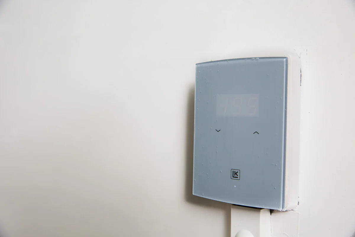Grijze LK thermostaat gemonteerd aan een witte muur op Laan van S-Gravenmade, met een afleesbare temperatuur van 19,5 graden.